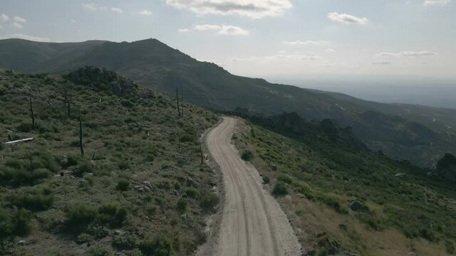 Winding dirt road leading over the mountains with short bushes and dead trees.