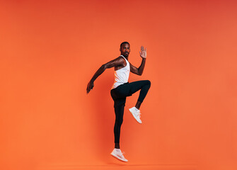 Fototapeta na wymiar Young fit man doing exercises in studio. Male athlete jumping in the air over an orange background.