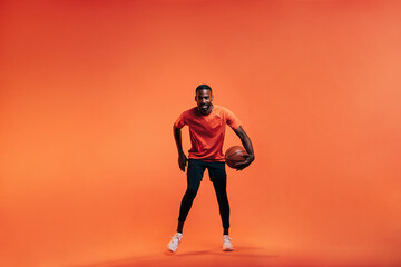 Fototapeta na wymiar Young sportsman dribbling basket ball in studio against an orange background