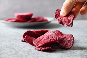 Take a piece vegetable beetroot chips on a gray background. Vegan snack. Close up.