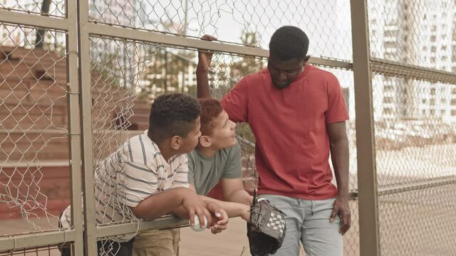 Medium shot of African American man talking to two teenage sons during outdoor baseball training at sportsground