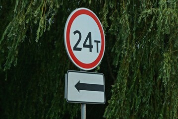 two road signs limiting the weight of 24 tons and an arrow on the street on a pole against a...