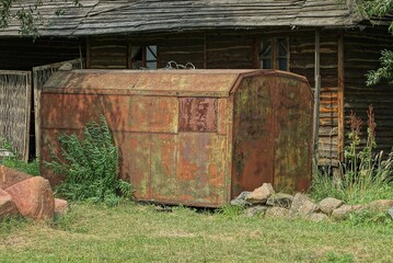 one big old iron trailer in brown rust on the street overgrown with green grass and vegetation