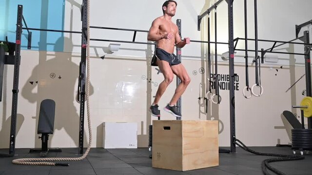 Slow-motion full shot of a fit young caucasian sportsman training alone doing box jump exercise in the gym. High quality FullHD footage.