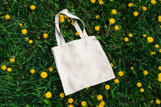 White cotton or mesh bag on dandelion grass background. Zero waste, no plastic, eco friendly shopping, recycling concept. Blank mockup shopper with place for artwork or text. Flat lay, copy space