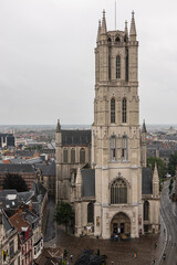 Gent, Flanders, Belgium - July 30, 2021: Historic medieval City hall building down from the Belfry with wide cityscape and skyline under gray rainy sky. Beige walls and black roofs.