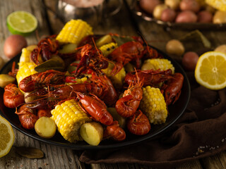 Boiled crayfish, pieces of corn and other vegetables are beautifully laid out on a large black platter. Ingredients in the background. Close-up. Restaurant, hotel, cafe, advertising.