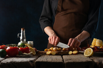 The cook prepares corn with crayfish, potatoes, lemon and other ingredients on the table. Delicious nutritious dish. Wooden texture. Restaurant, hotel, advertising.