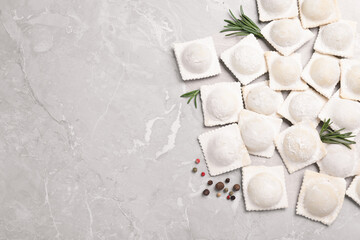 Uncooked ravioli, rosemary and peppercorns on grey marble table, flat lay. Space for text