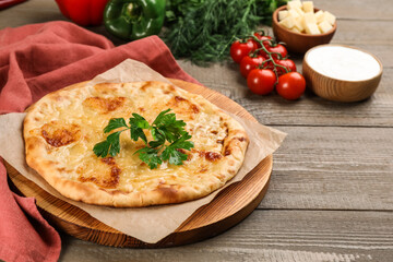 Delicious khachapuri with cheese, parsley and vegetables on wooden table