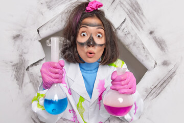 Crazy female nerd scientist biochemist works on chemical experiment holds glass flasks with...