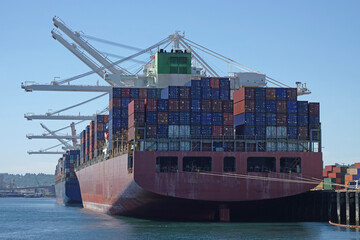 Two large, nondescript container ships are shown dock in a port next to industrial cranes.