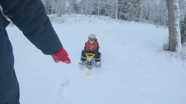 Hand Pulling A Sled On Snow With Son Riding At Winter In Sweden. handheld shot