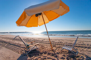 Two beach chairs with yellow umbrella on the beach in the early morning.