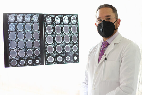 Medical Doctor Specialized In Neurology With A Mask And A Gown Uniform Reviews X-rays Of The Brain Or CT Scans As His Professional Work
