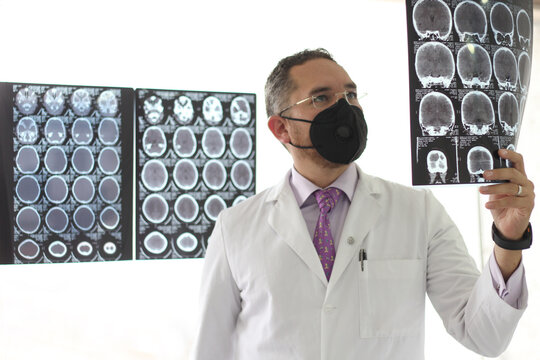 Medical Doctor Specialized In Neurology With A Mask And A Gown Uniform Reviews X-rays Of The Brain Or CT Scans As His Professional Work
