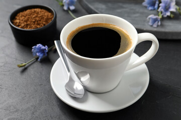 Cup of delicious chicory drink and flowers on black table, closeup