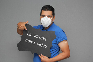 Latino adult man shows his arm that just received the Covid-19 vaccine and a sign that says 