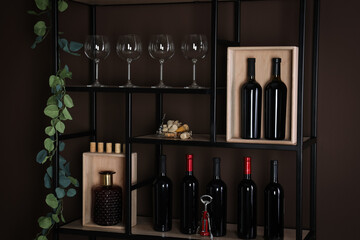 Rack with bottles of wine and glasses near brown wall