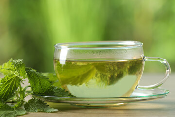 Glass cup of aromatic nettle tea and green leaves on table, closeup