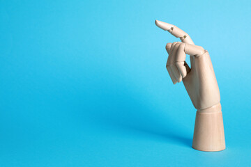 Wooden mannequin hand on light blue background. Space for text