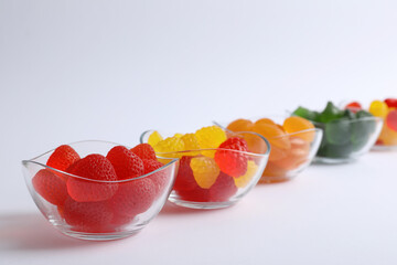 Different delicious gummy candies in bowls on white background - obrazy, fototapety, plakaty