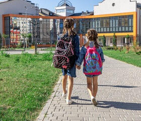 Two little girls go to school, holding hands, back view.