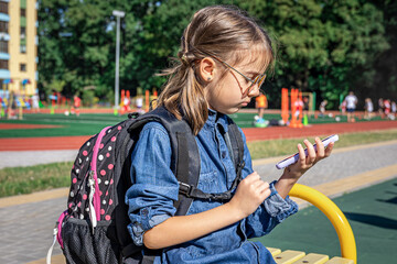Obraz premium A little girl, a primary school student in sunglasses with a phone in her hands.