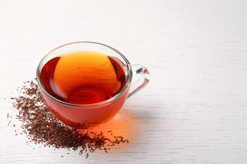 Freshly brewed rooibos tea and scattered dry leaves on white wooden table. Space for text