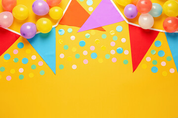 Bunting with colorful triangular flags and other festive decor on yellow background, flat lay....