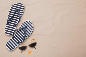 Pair of striped flip flops, sunglasses and sea shells on sand, flat lay. Space for text