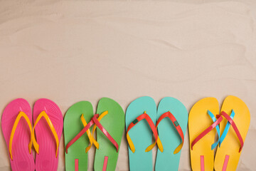 Different bright flip flops on sand, flat lay. Space for text