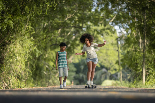 Childhood and leisure activity - African American curly hair children training skateboard togetherness on the road at park.