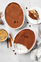 Classic Italian Dessert Tiramisu topped with cocoa  in a ceramic dish. Light gray background. top view