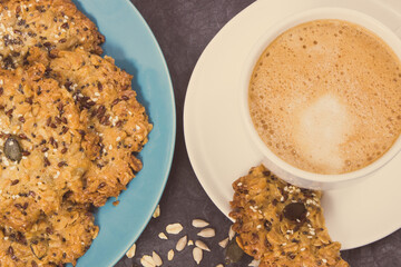 Cup of white coffee and fresh baked oatmeal cookies with honey and healthy seeds. Delicious crunchy dessert