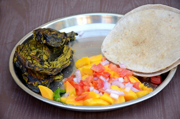 closeup the brown unleavened bread with fried arabic leaves vegetable made and sliced mango,onion,tomato,chilly over out of focus brown background.