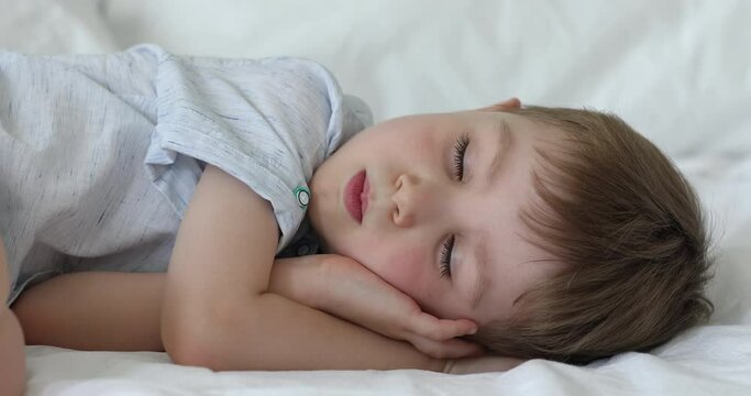 Close up little five years old cute boy lying in bed with eyes closed, serene kid sleep on white bedding enjoy healthy day nap and comfy memory foam mattress, sweet dreams, health care, growth concept