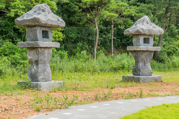 Two large stone carved lanterns beside concrete walkway in rural public park.