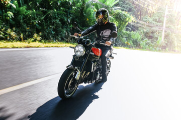 Caucasian man in a black helmet rides classic motorcycle on the road among summer tropics and looks at camera. Lifestyle or hobby of grown up man