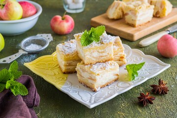 Sliced apple pie made from shortcrust pastry with cottage cheese cream and apple wedges on a square plate on a green concrete background. Apple pie recipes.