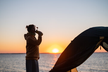Woman resting in a tent in nature at sunset. The girl set up camp on the river bank