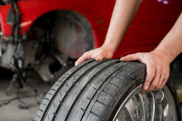 An auto mechanic holds a wheel of a car. Change of car tires according to the season