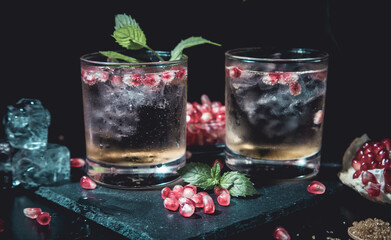 two moody summer cocktails with mint, pomegranate and ice cubes on a black background