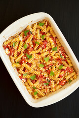 Homemade Baked Feta Tomato Pasta in a baking dish on a black surface, top view. Flat lay, overhead, from above.