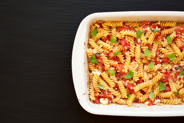 Homemade Baked Feta Tomato Pasta in a baking dish on a black surface, top view. Flat lay, overhead, from above. Space for text.