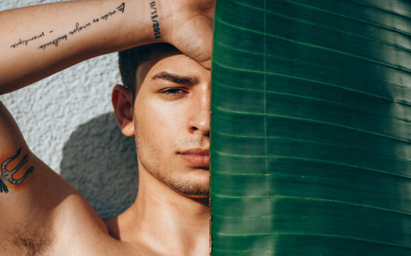Young man fashion art portrait. Handsome male close up. Portrait of sexy muscular guy, looking at camera. Fashion urban boy posing with banana leaf