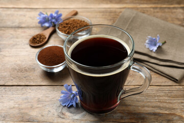 Glass cup of delicious chicory drink and flowers on wooden table, closeup