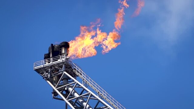 Oil and gas. Slow motion of gas flare from bottom burning at oil and gas platform with background blue sky and clouds.