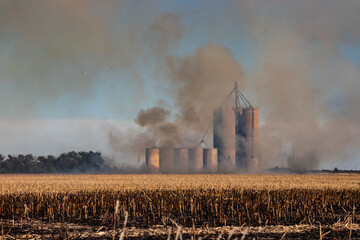Wide angle landscape shot of a silo in a burning agriculture field of crops