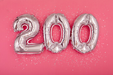 From above of silver shiny balloons demonstrating number 200 on pink background with scattered glitter - obrazy, fototapety, plakaty